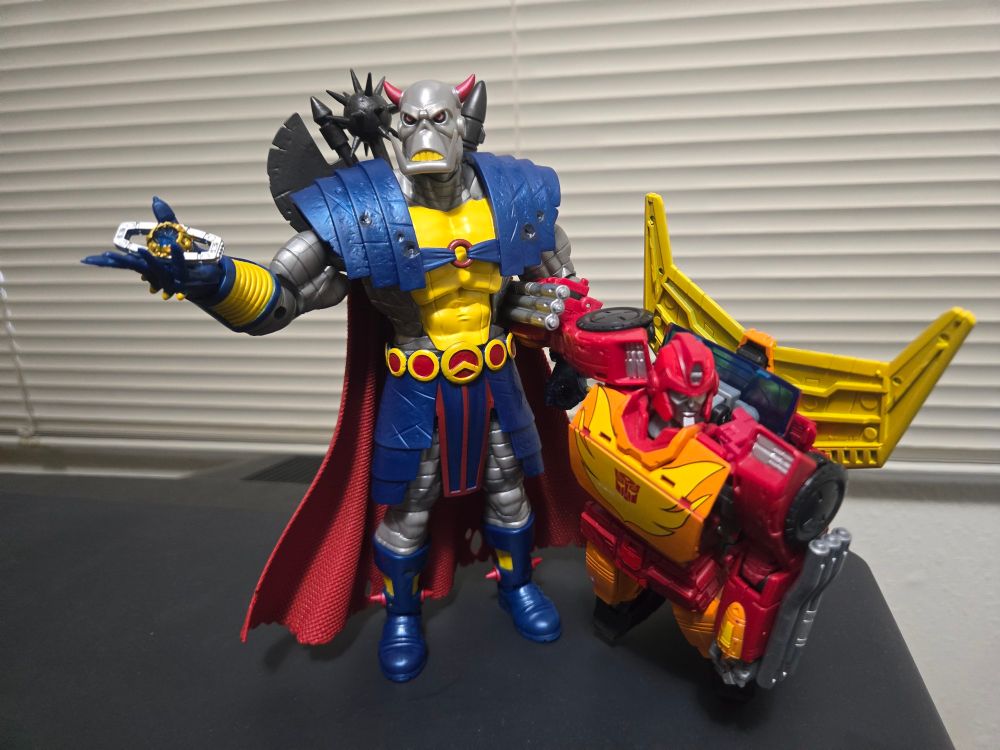 The 2024 Marvel Legends figure of Death's Head holding the Matrix of Leadership in his right hand and, in his left arm, an incapacitated Rodimus Prime from the War For Cybertron: Kingdom. The composition is in reference to The Transformers (Marvel UK) #151, "The Legacy of Unicron!", page 7, panel 5.