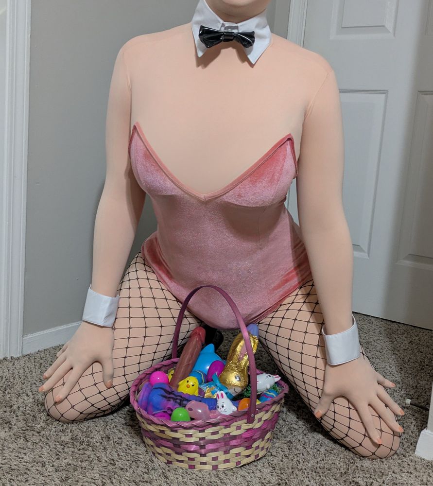 Natalie dressed up in a pink, velvet bunnysuit, with accessories like cuffs, fishnets, and a collar to complete the bunnygirl look. She's knelt on the floor, a wicker basket between her spread legs. The basket is filled with traditional Easter goods, like plastic eggs and a chocolate bunny, but along with these goods are dildos and other sexual toys, including a chastity cage and lube.

While knelt, Natalie is leaning forward over the basket, hands on her thighs.