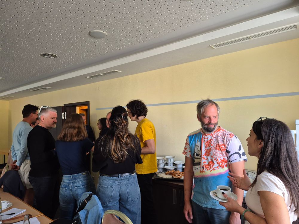 A group of 9 scientists in casual dress standing having a discussion over cups of tea.