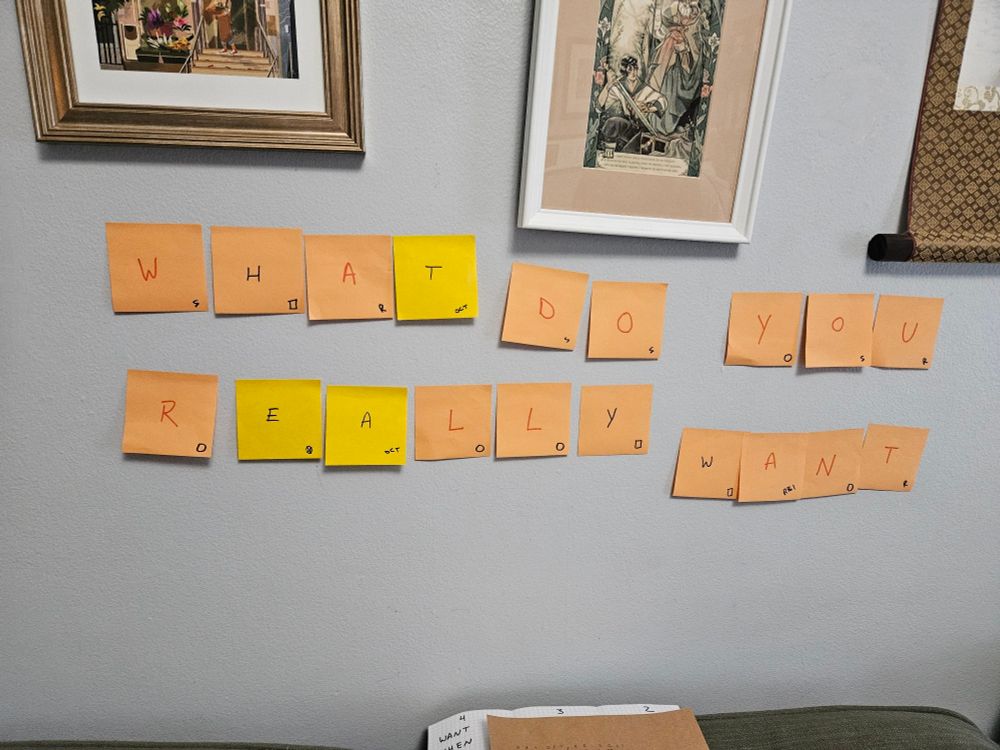 A series of orange and yellow post it notes on a blue wall that spell out "what do you really want"