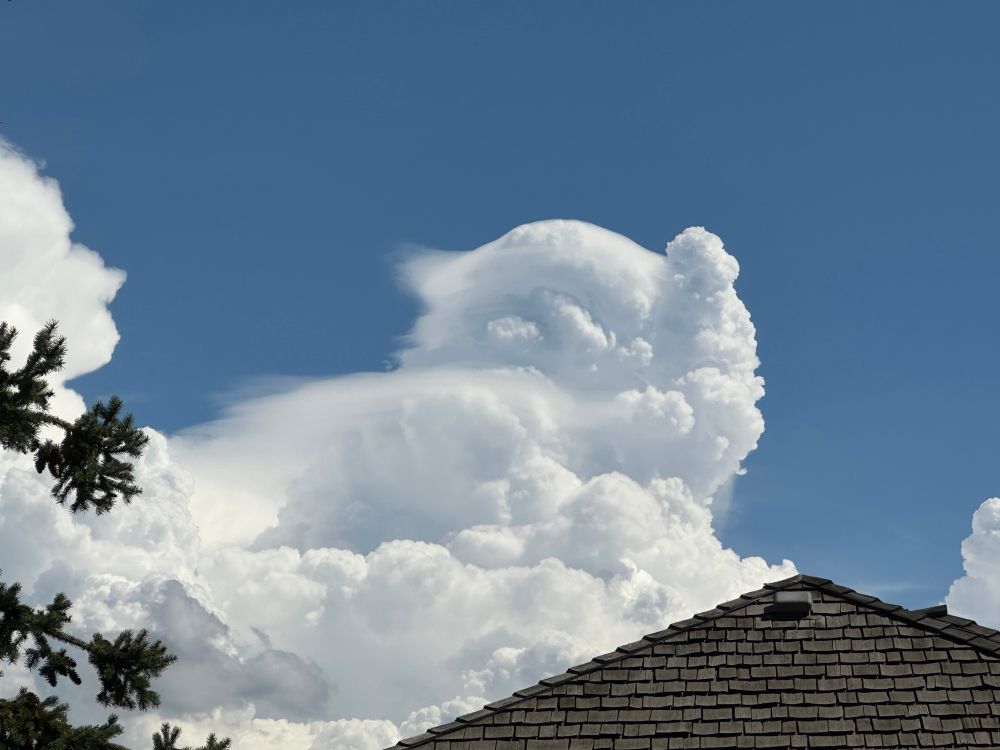 A picture of clouds over a peaked roof. The shape of the clouds is vaguely sphinxian with  parts trailing off the top reminiscent of flowing hair