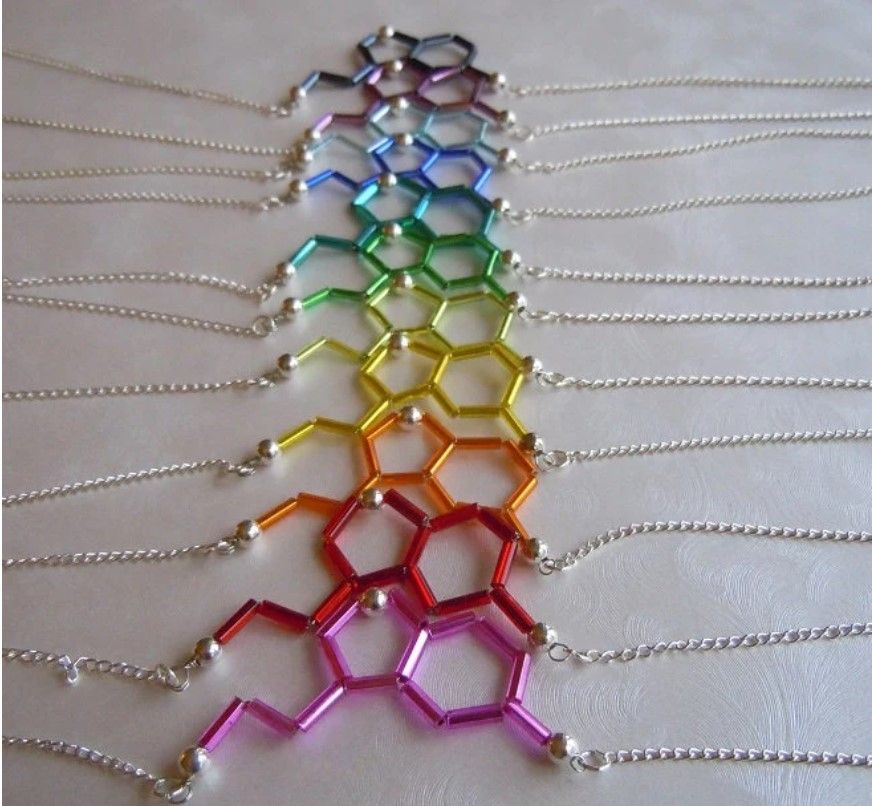 Beaded serotonin molecule necklaces in charcoal, purple, light blue, blue, teal, true green, lime green, yellow, orange, red, and pink.