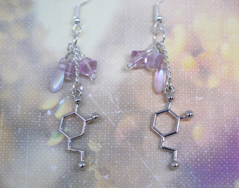 Dangle charm earrings. A silver tone dopamine charm hangs on a chain with light pink beaded accents. 