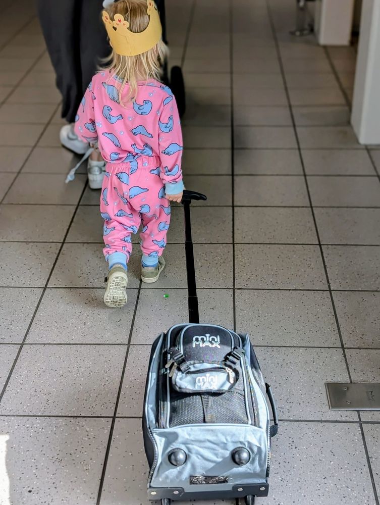 A toddler in pyjamas walking with a rolling suitcase through an airport 