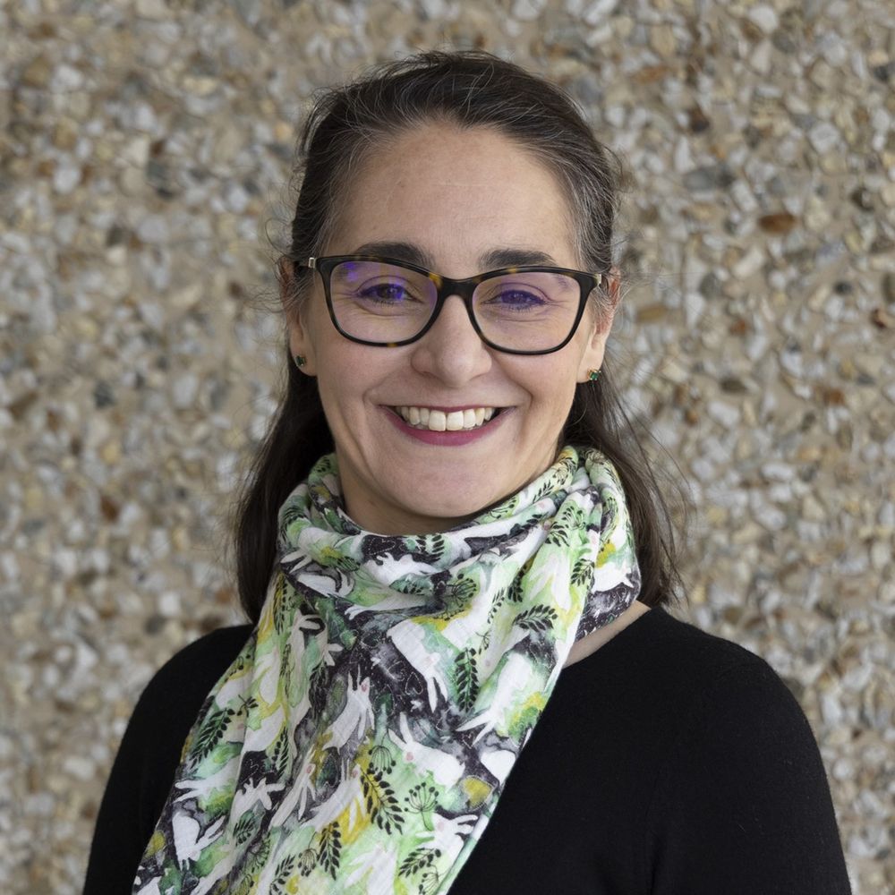 Headshot of a smiling woman wearing glasses and a patterned neck scarf