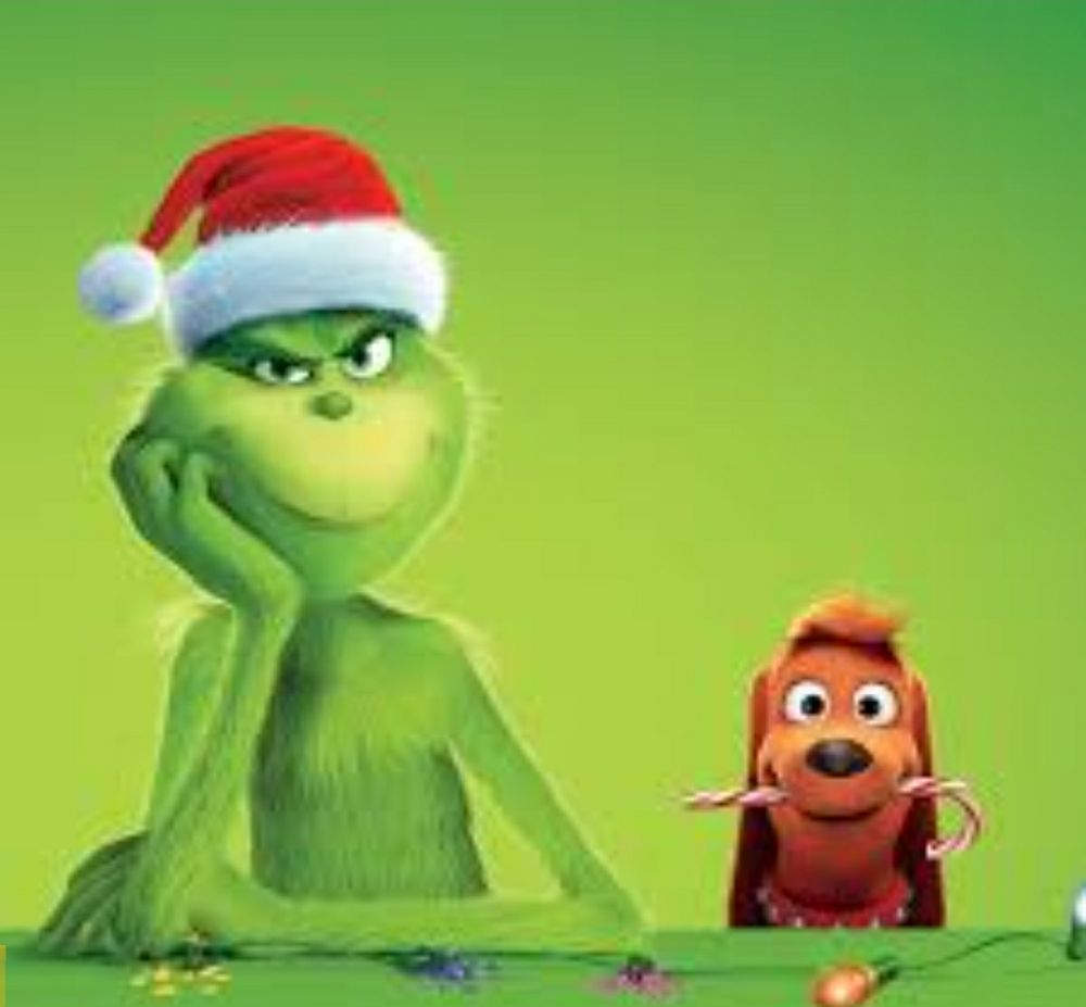 Picture shows the Grinshill wearing a red santa hat with head leaning on his hand. He is with his dog. The dog has a candy cane in its mouth. There's a string of Christmas lights in front of them.