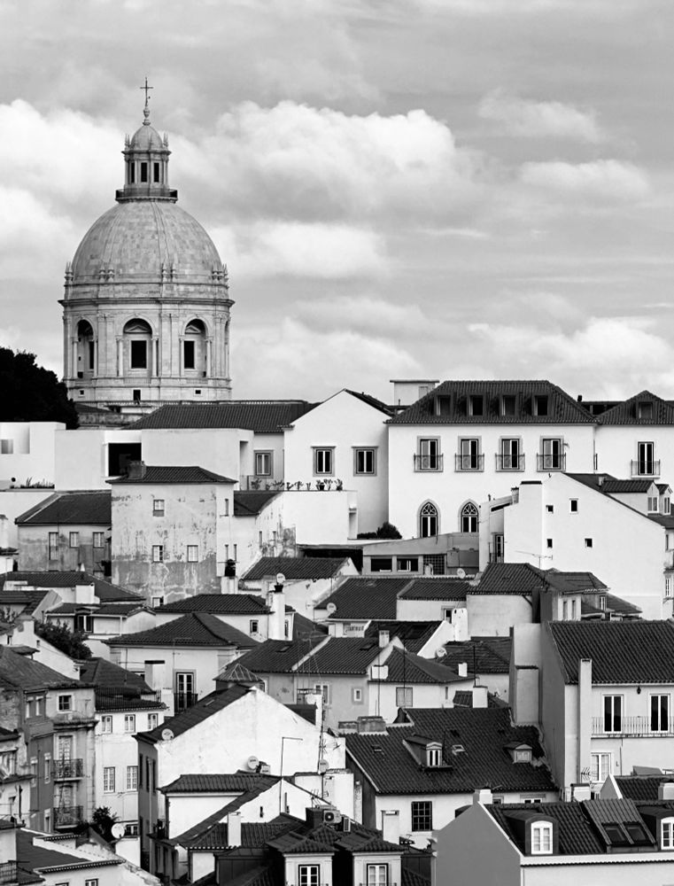 Black n White photo of a hill of buildings, with a domed structure at the top. Fluffy white clouds.
