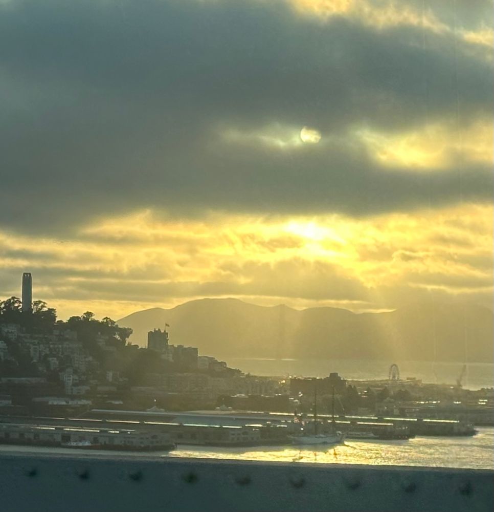 Photo looking into the sun through broken clouds of fog, leaving rays of sunshine coming down on skyline of San Francisco and the bay