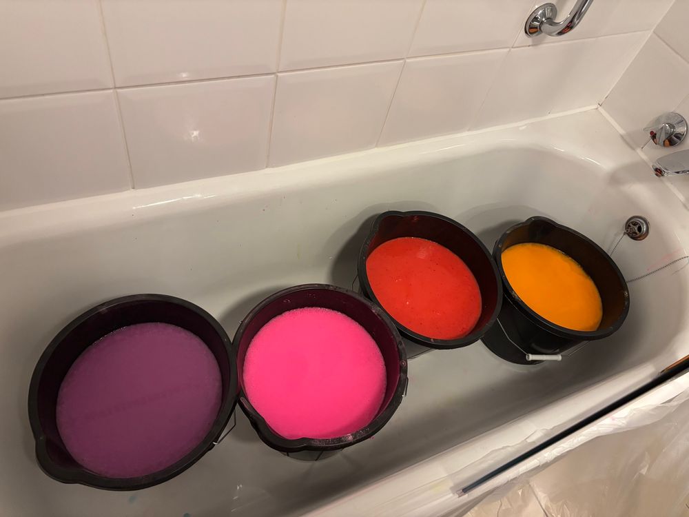 4 buckets of gunge in a bathtub, from left to right: purple, pink, red, orange