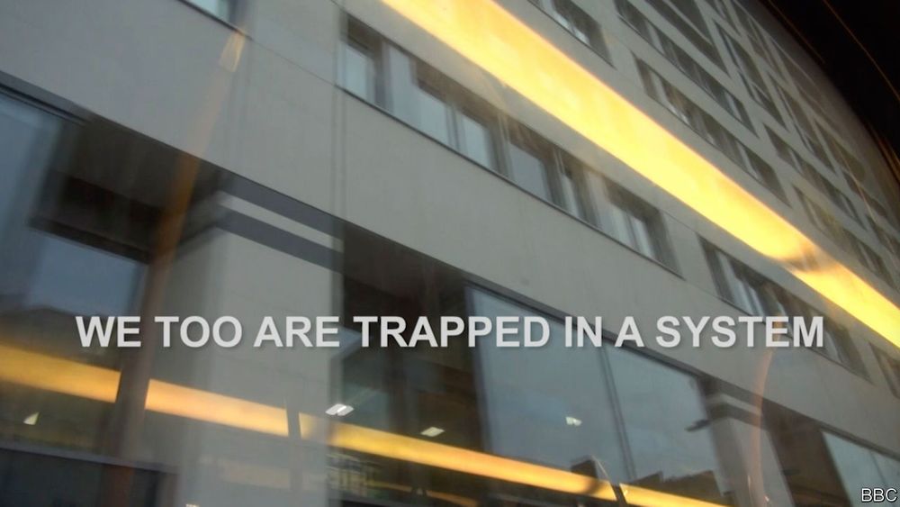 Adam Curtis Title Card: We Too Are Trapped In A System. Text over a background of a large office building