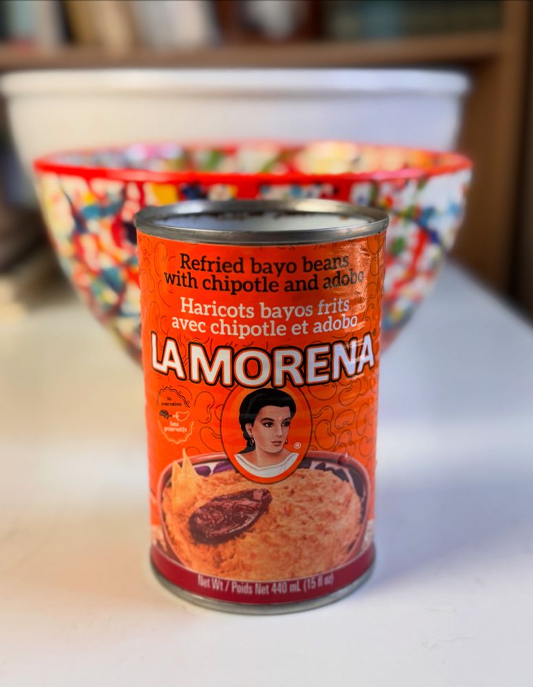 A beautiful orange can label with a brunette woman in cameo above a pan of refried beans, and the company name, La Morena, above the woman.