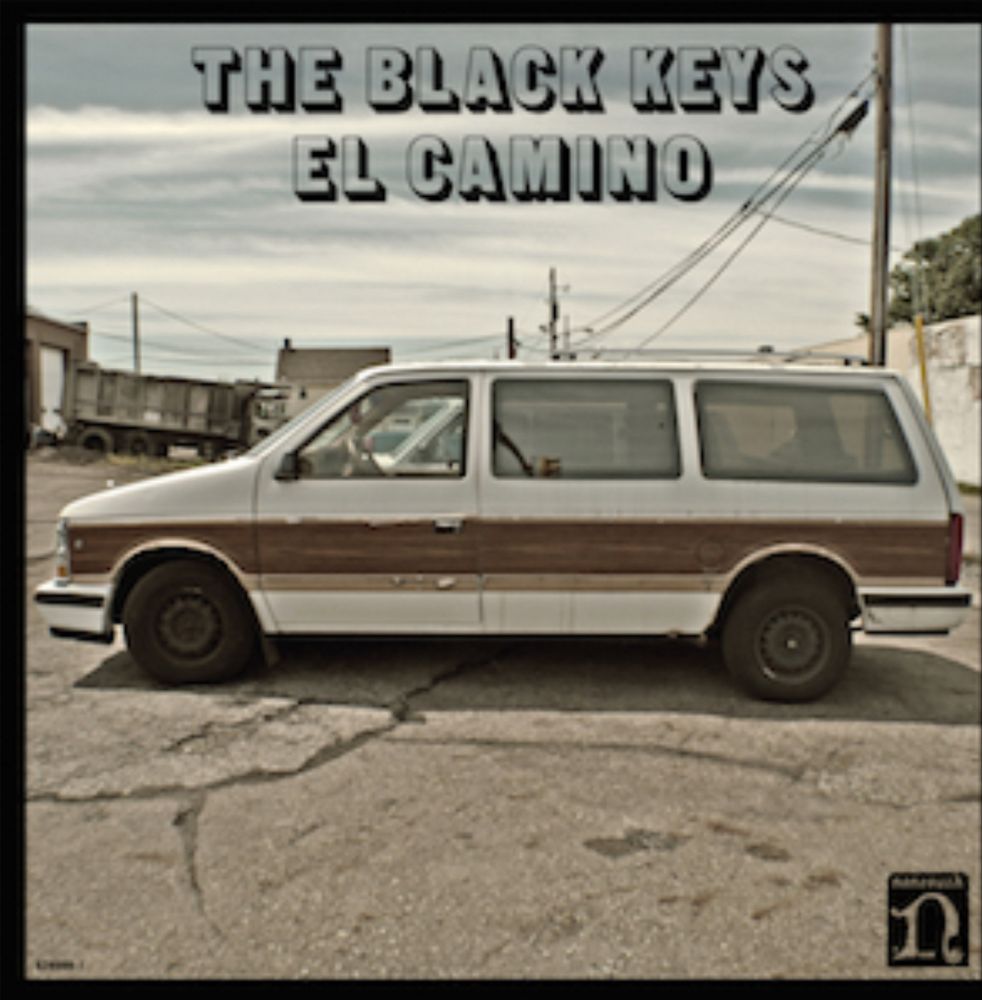 A side view of a white faux wood-sided minivan parked in an old  parking lot.