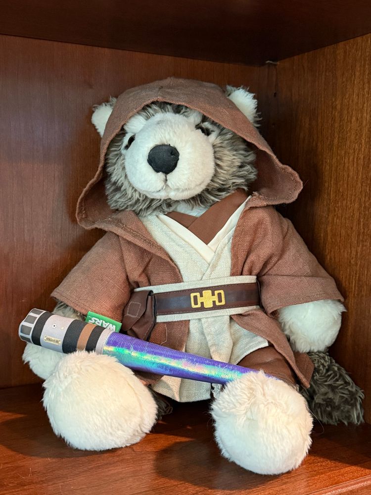 Picture of a Build-a-Bear stuffed toy wolf wearing a Jedi costume and holding a blue light saber. 