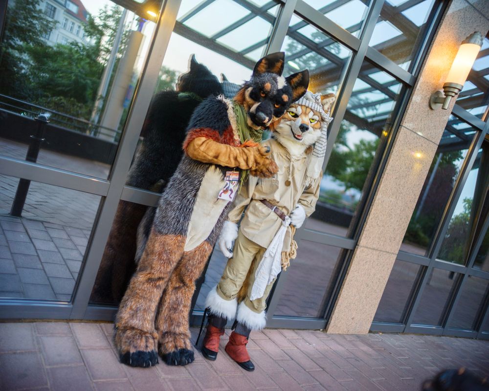 Wolf and Blue Heeler fursuiter (the former dressed as a proper pirate) posing next to each other in front of a glass facade.