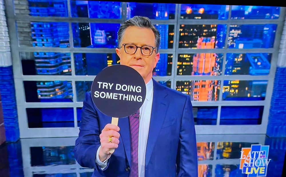 Stephen Colbert holding a sign saying “Try doing something”