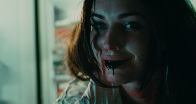 megan fox in jennifer’s body (2009) throwing up near black blood. she is smiling as blood drips from her mouth, her hair is down 