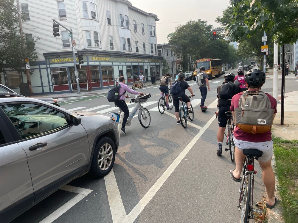 Five bike/micromob riders queued outside the bike lane at a red light, another five or so in the bike lane