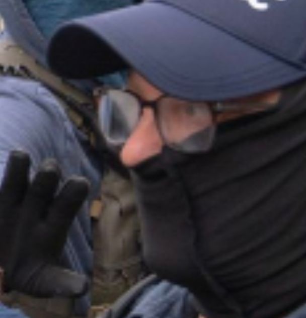 ICE dweeb wearing a black gaiter pulled tight against his nostrils, but below the tip of his protruding nose.