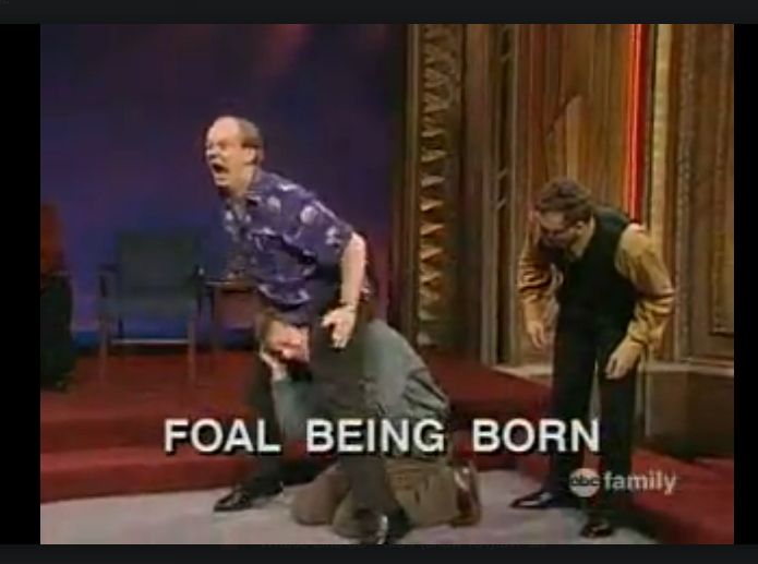 A screenshot of a scene from early Whose Line is it Anyway with Ryan Styles crawling between Colin Mochrie's legs with Greg Proops staring on in horror and the text "FOAL BEING BORN" across the screen.