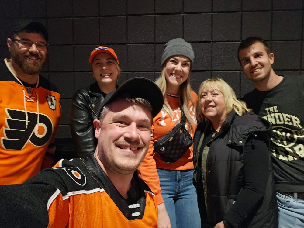 A group selfie with me in the front and five people behind me. From left to right, they are: a tall bearded man in a Flyers jersey (Matt), a woman in an orange hat and a leather jacket (Rin), a tall woman in an orange shirt and a gray beanie (Lex), a woman in a black vest with blond hair (my mom), and a tall man in a band shirt (my German friend)