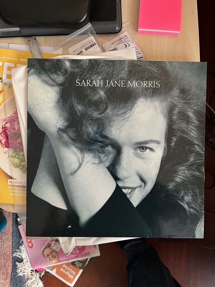 LP record on desk. Sarah Jane Morris album. Cover is a portrait of Sarah Jane smiling her face partially obscured by her hair and arms.