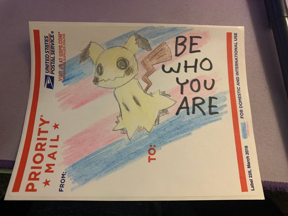 drawing on a priority mail sticker, of the pokemon, mimikyu, over a trans flag. written next to it, "BE WHO YOU ARE".