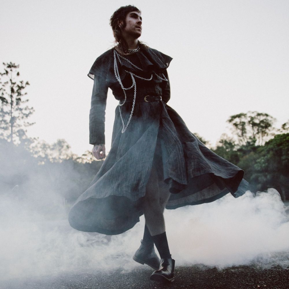 a man in a dark elegant gown captured spinning around as smoke billows around his ankles, it is an album cover and its giving DRAMA