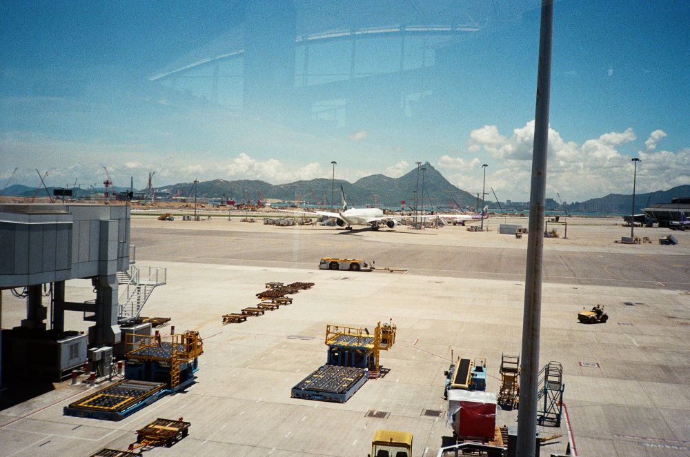 A scene from out the window at Hong Kong Airport. Mountaintops and airport machinery. There are some reflections coming from inside the terminal