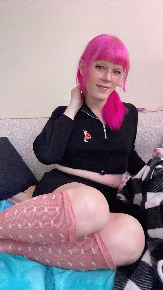 me sitting on the couch wearing my compression socks but they’re rose pink with polka dots, also wearing a black tennis skirt & black long sleeved crop top