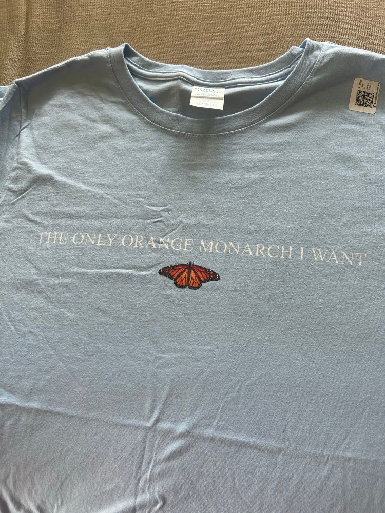 A blue T-shirt with a small monarch butterfly on it. Above the butterfly it says “The Only Orange Monarch I Want”