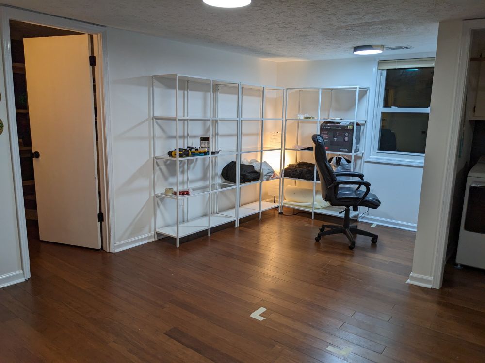 The corner of a finished basement with white shelves. The shelves have some miscellaneous items on them.