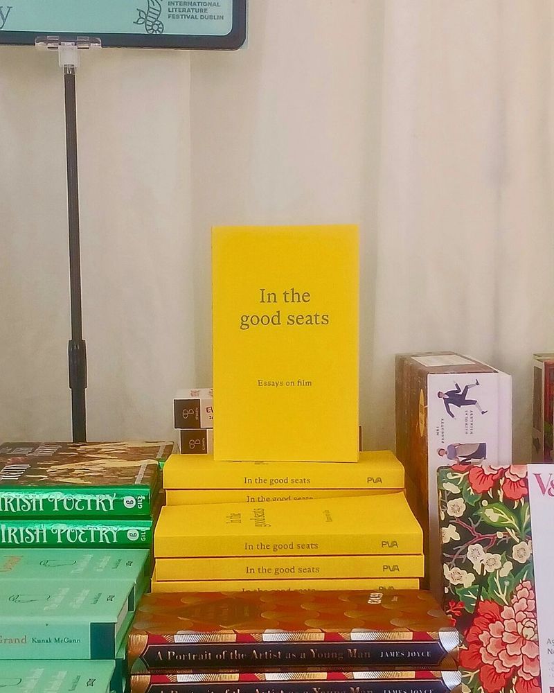 Image description: A stack of PVA Books' latest title, In the good seats: Essays on film, sits alongside other festival titles in ILFD's festival bookshop.