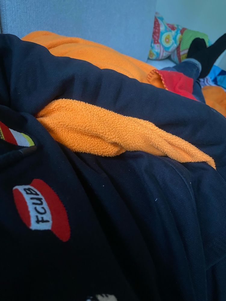 Person im schwarzen Hoodie liegt mit oranger Decke auf einer Couch.