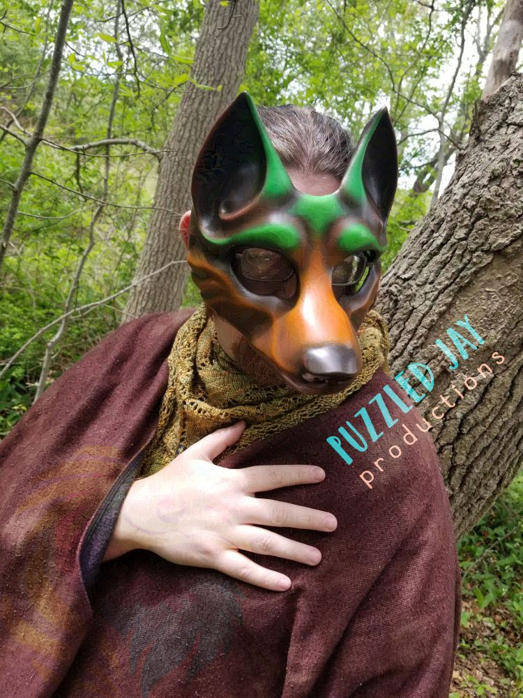 people wearing a brown and green wolf mask peer around trees