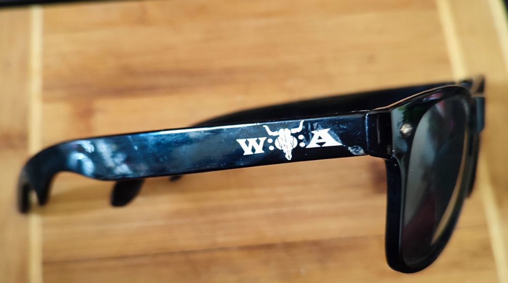 Schwarze Sonnenbrille mit Wacken Logo und Flaschenöffner am Ende der Bügel 