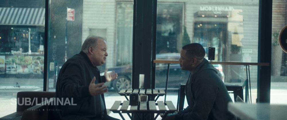 Tom McGowan gestures while speaking to Ryan Jamaal Swain in a coffee shop.