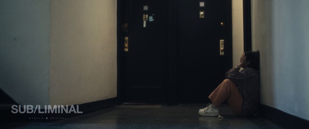 Geena Quintos sits against a wall of a hallway with her head in her hands.
