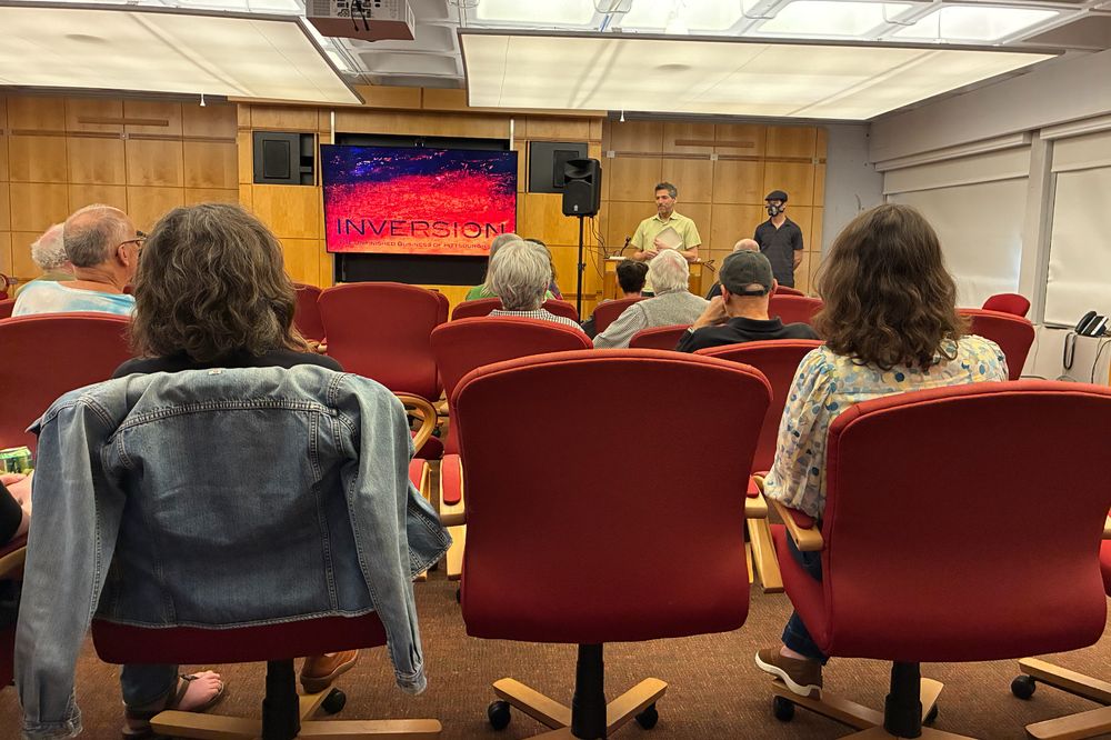 Will Zavala, organizer of the Pittsburgh Documentary Salon, introducing Mark Dixon at the beginning of the event. "Inversion" opening image is at the front, with several audience members in chairs looking on. 