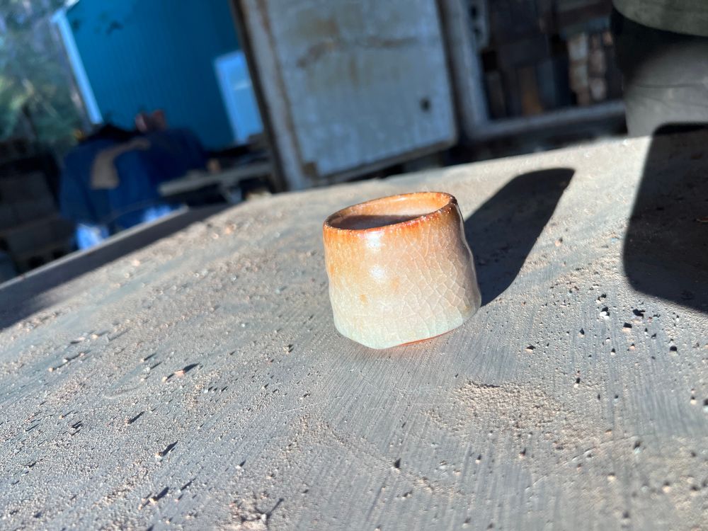 Small tea cup in a white shino style glaze that breaks orange at the rim