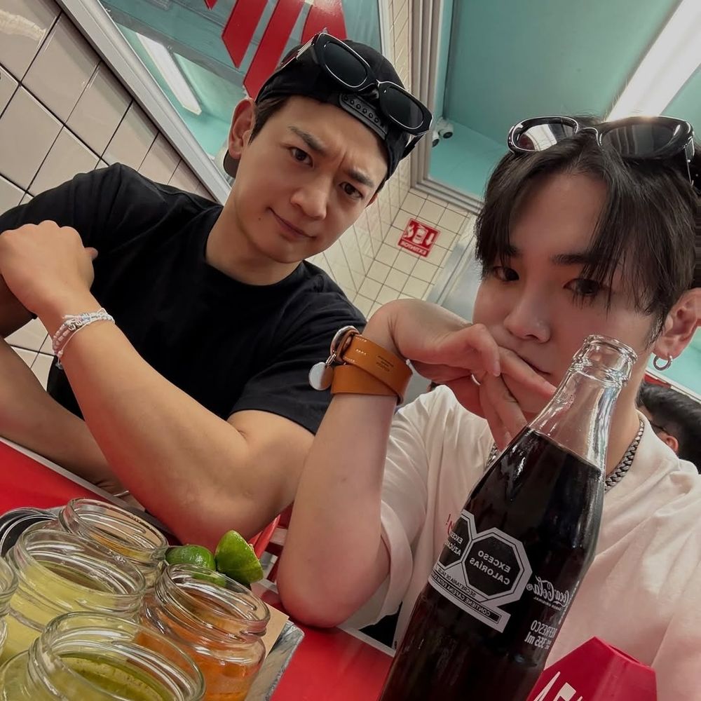 Minho and Key from SHINee, sitting at a table with drinks, smiling and enjoying their time together.