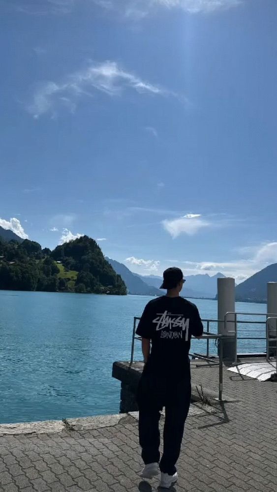 Minho from SHINee stands on a dock, gazing thoughtfully at the water under a clear sky.