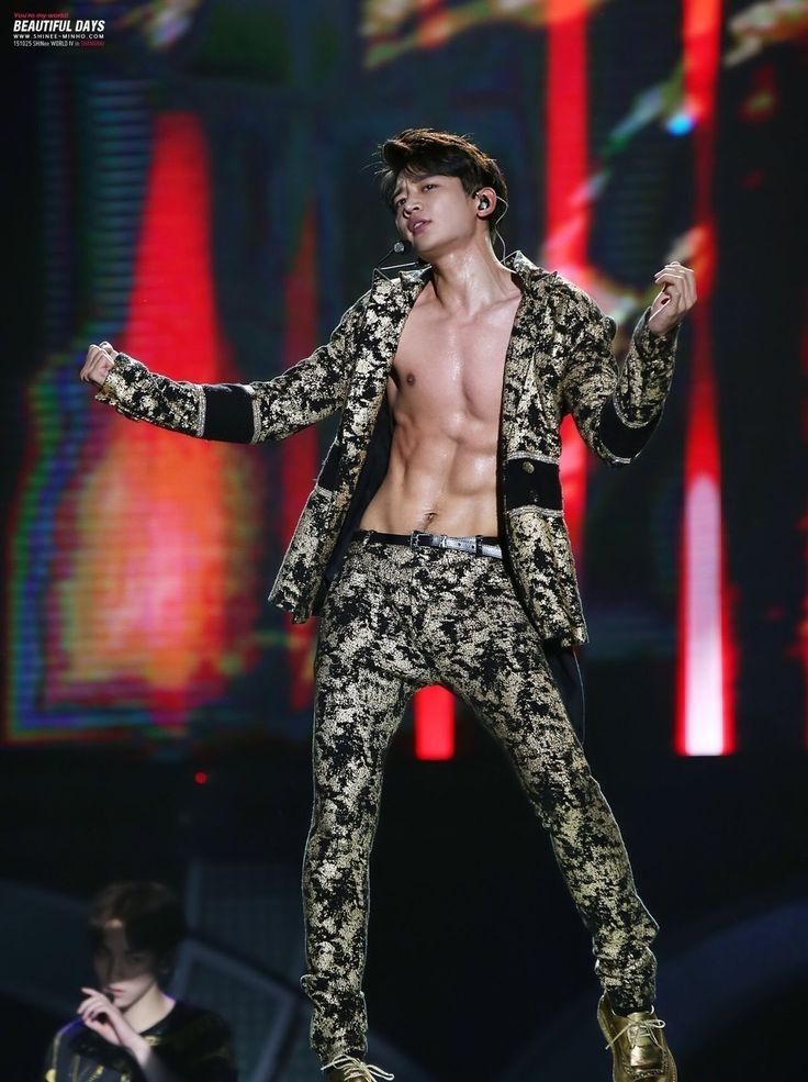 Minho from SHINee, shirtless and in a gold and black suit, captivates the audience with his performance on stage.