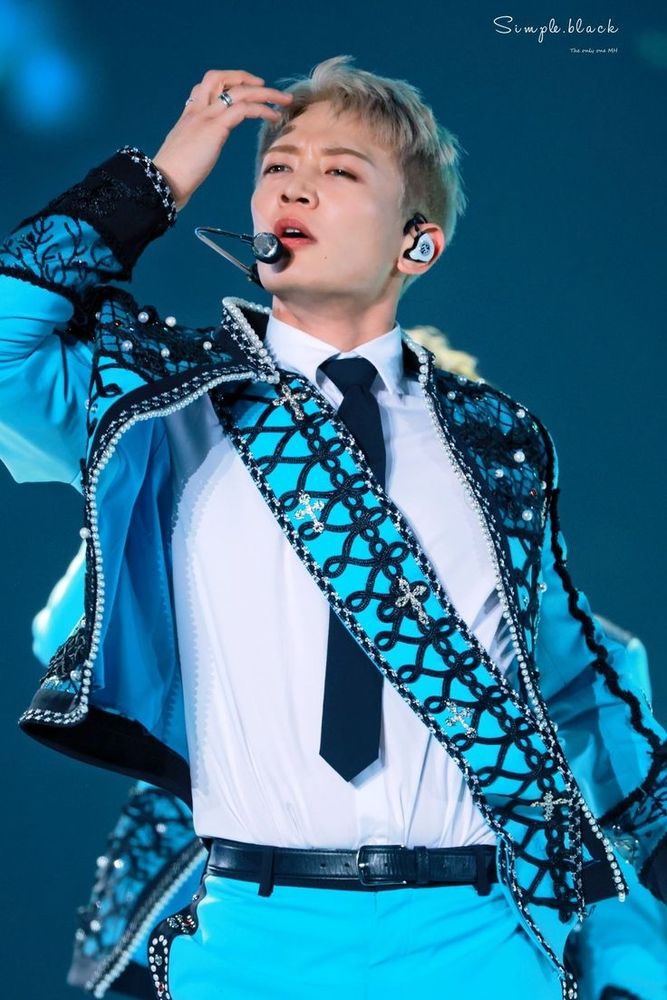Minho from SHINee dressed in a blue suit and white shirt, singing passionately during a live performance.