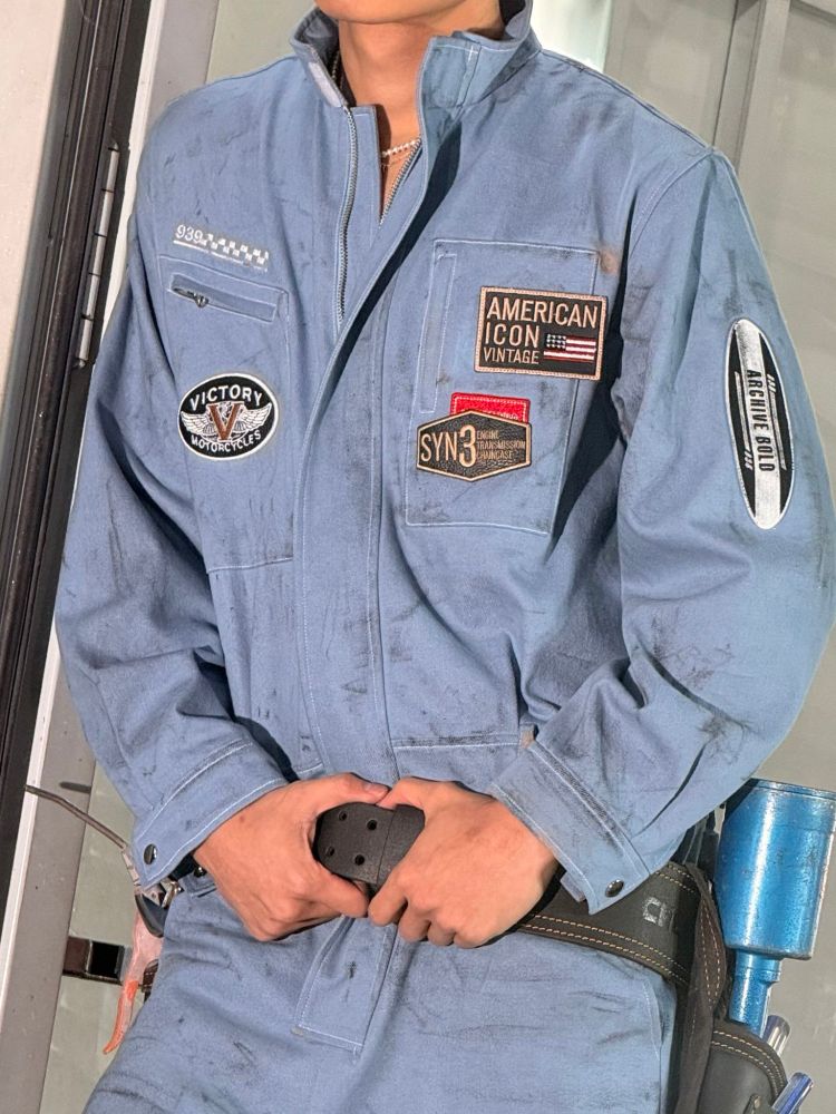 A man in a blue work suit, Minho from SHINee, stands next to a door