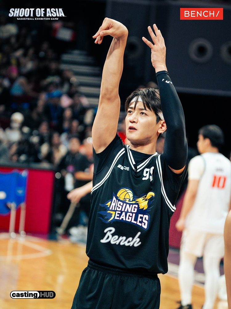 Minho from SHINee in a black jersey holds up his arm, after throw a ball.