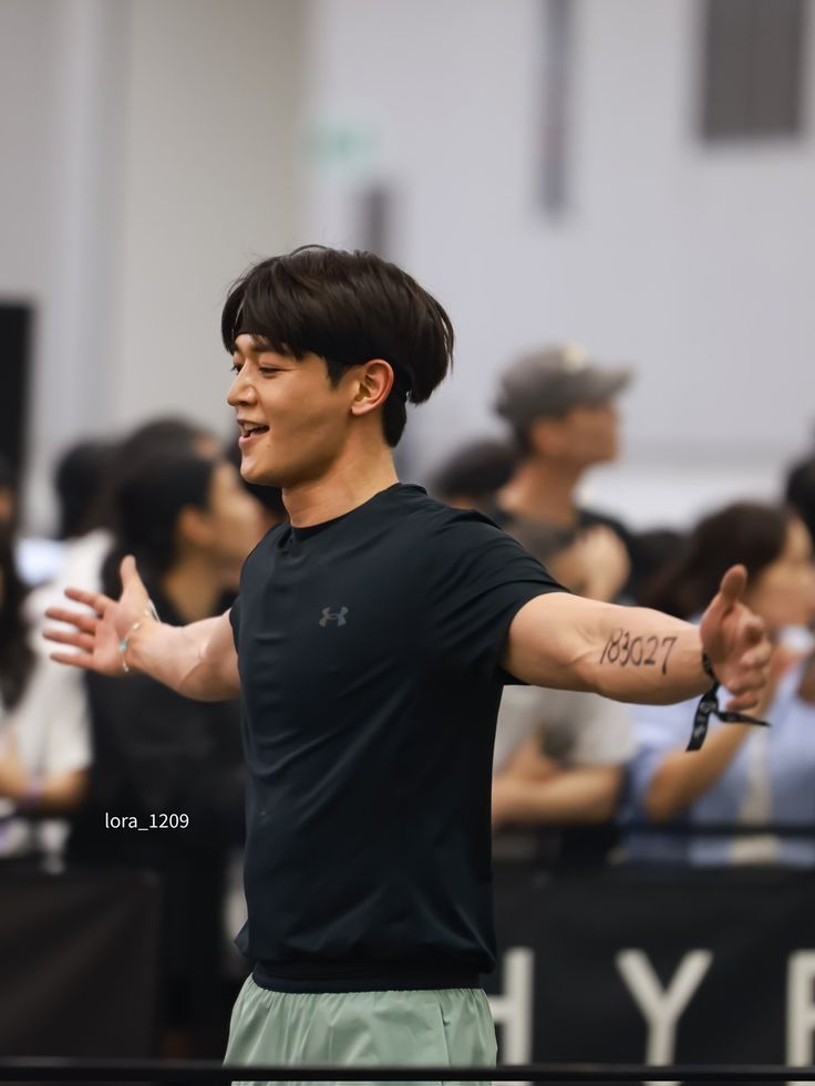 Minho from SHINee, stands with open arms, smiling.