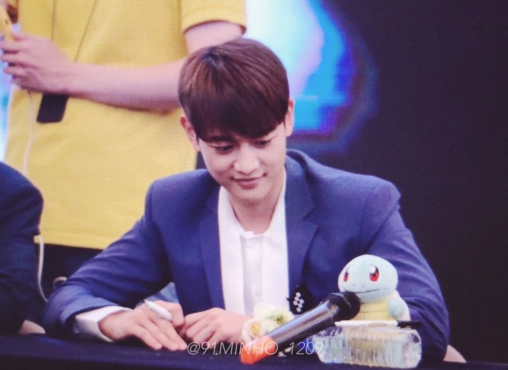 Minho from SHINee, dressed in a suit, signs an autograph while gazing at Squirtle at a fansign.