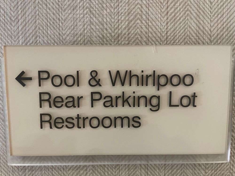 A directional sign on a wall: < Pool & Whirlpoo Rear Parking Lot Restrooms