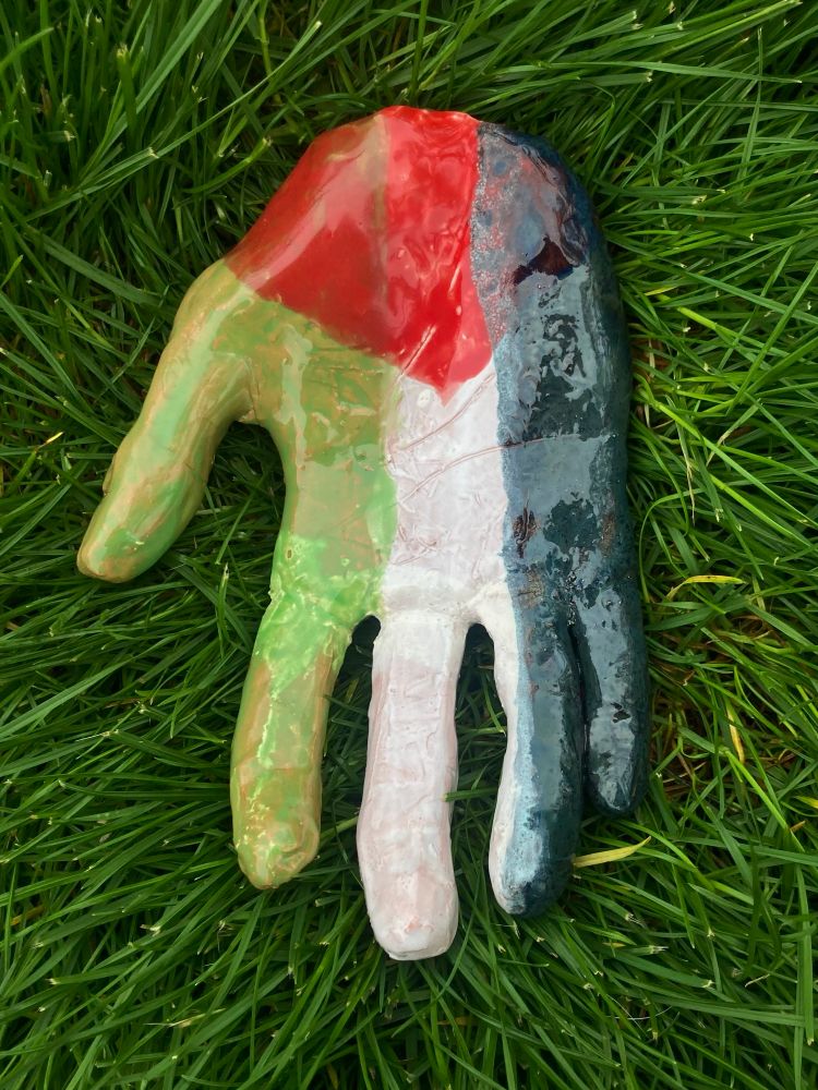 A picture of a ceramic hand lying in the grass, painted to resemble the Palestinian flag