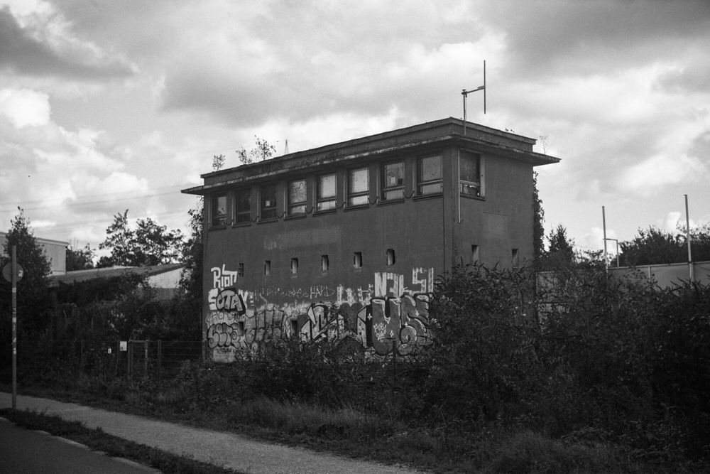 Black and white photo of an abandoned signal box next to a former railroad track, now used as a bikelane and footpath.